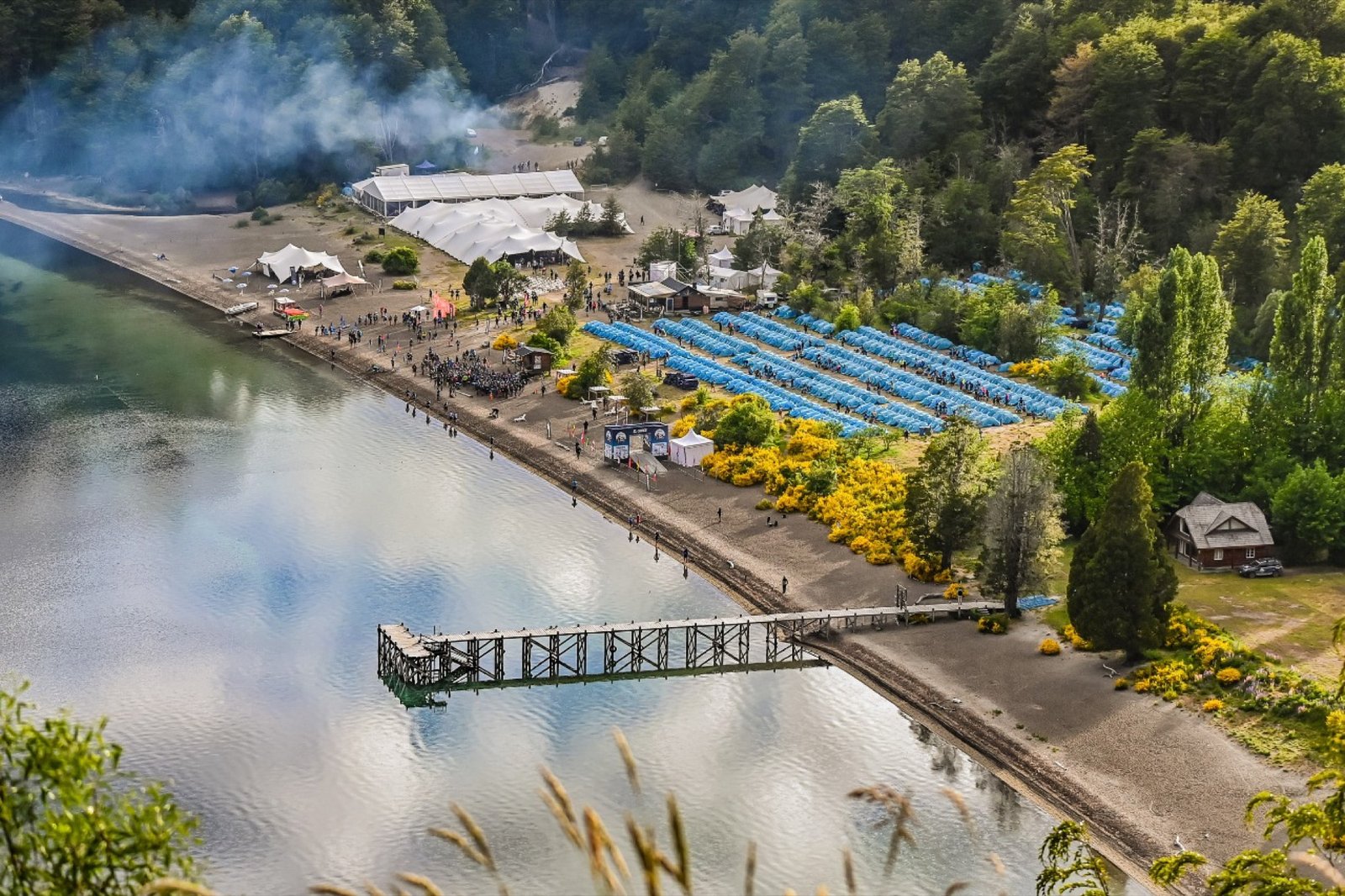 Vista aérea del campamento a orillas del lago, con el muelle y las carpas azules
