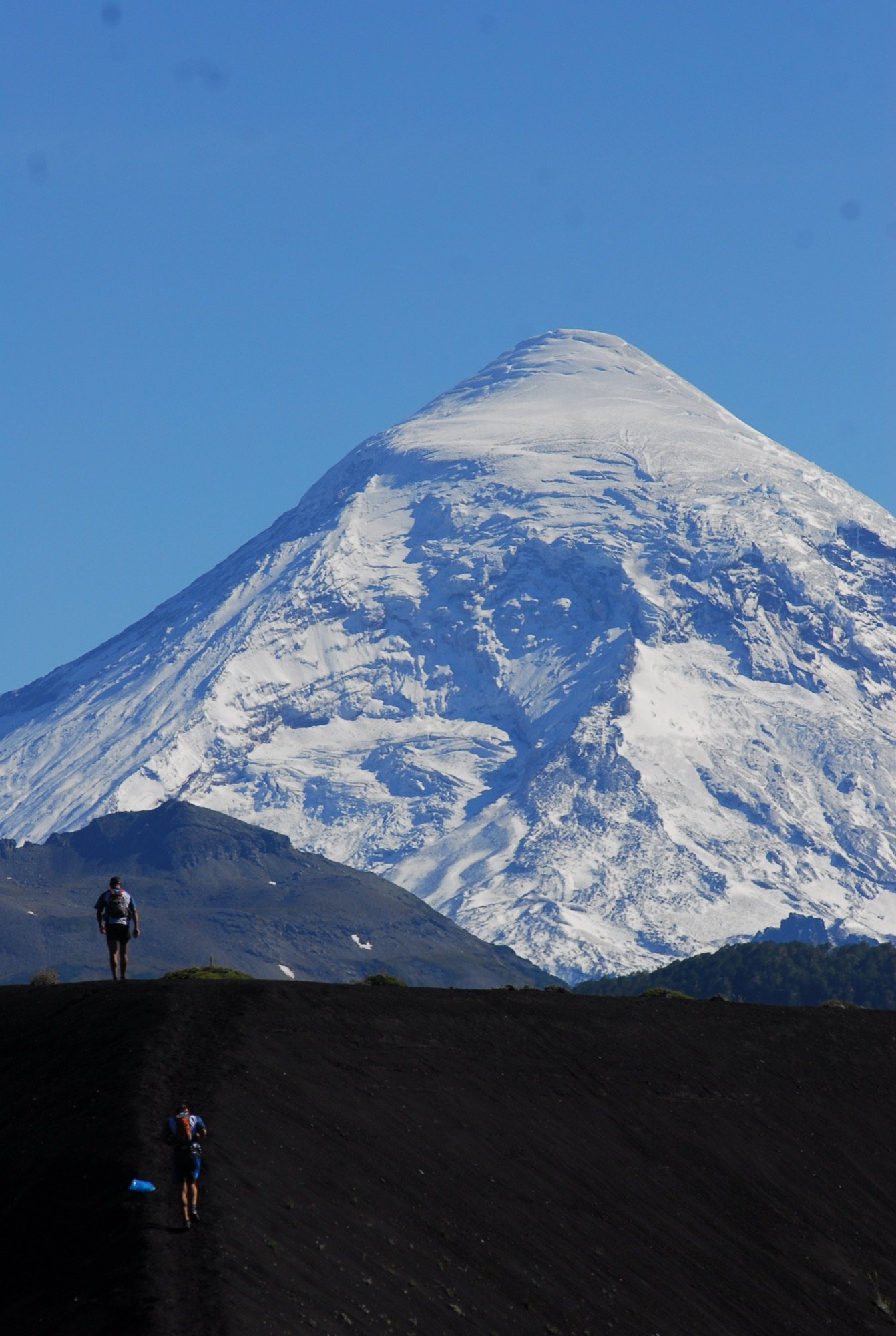Un volcán nevado visto desde abajo, con un corredor diminuto en primer plano